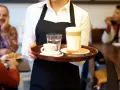 Kelnerka niesie tacę z kawą i wodą. Zastanawiasz się, ile zarabia barman w Sopocie?