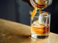 Idealny moment, by drink whisky z colą. Bursztynowy płyn z lodem i skórką pomarańczy.