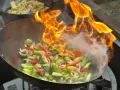 Pyszny stir-fry przepis w akcji! Warzywa w woku płoną żywym ogniem, tworząc apetyczny dym.
