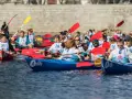 Zawodnicy w łodziach, jeden w masce konia, rywalizują w wyścigu. Wódka z Red Bullem i wódka z sokiem pomarańczowym to napoje, które mogą dodać energii.