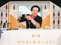 Barman Grzegorz Pikuła, w stylowym kapeluszu, nalewa drinka. W tle półki z butelkami whisky, idealne dla miłośników krwawych mary.