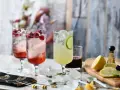 Orzeźwiający drink z fantą i malinami, obok drink z limonką i miętą. Na desce cytryny, limonki i tarka.