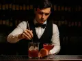 Barman miesza drinka, zastanawiając się, ile zarabia barman za granicą. W tle półki z butelkami.