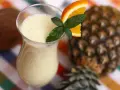 Orzeźwiający drink z ananasem, ozdobiony plasterkiem pomarańczy i miętą, na tle całego owocu.