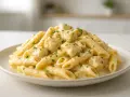 Penne z sosem serowym, posypane natką pietruszki, prezentują się apetycznie na białym talerzu.