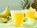 Orzeźwiający koktajl z ananasa i banana, idealny na upalne dni. Obok leżą świeże owoce i złote łyżeczki.