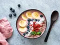 Kolorowy smoothie bowl z bananem, jagodami i kokosem, przypominający wyglądem tradycyjny kisiel. Obok leży drewniana łyżka i różowa serwetka.