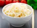 Biały makaron w misce, przypominający makaron konjac lub makaron z alg, z pomidorami i zielonymi warzywami w tle.