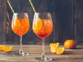 Dwa orzeźwiające drinki z aperolem, ozdobione plastrami pomarańczy i słomkami, na drewnianym blacie.