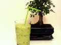 Orzeźwiający koktajl z kiwi i banana, z zieloną słomką, obok miniaturowego drzewka bonsai.