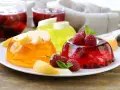 Kolorowe galaretki z owocami: pomarańczowa z brzoskwiniami, żółta z bananem, czerwona z malinami i porzeczkami. Idealne, gdy dodać owoce do galaretki, by była pyszna.