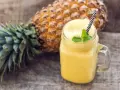 Orzeźwiający koktajl z ananasa i banana, ozdobiony miętą, na drewnianym tle.