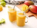 Orzeźwiający drink z wódką mango, podany w słoiczkach z metalowymi słomkami, obok świeżych owoców mango i limonek.