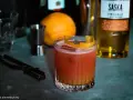 Orzeźwiający drink z likierem pomarańczowym, ozdobiony skórką cytrusową. Obok pomarańcza i butelka Saska.