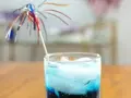 Niebieski drink z lodem i parasolką, przypominający letni koktajl z blue curacao.