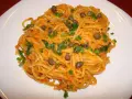 Pyszne spaghetti z tuńczykiem i kaparami, posypane szczypiorkiem, na białym talerzu.