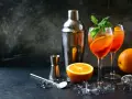 Orzeźwiający aperol z szampanem, udekorowany pomarańczą i miętą, gotowy do podania. Obok shaker i akcesoria barmańskie.