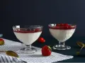 Dwie panna cotta: jedna na śmietance z borówkami, druga na jogurcie z malinami. Obok świeże truskawki i złote łyżeczki.