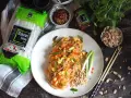 Gotowy Pad Thai przepis na talerzu, obok makaron ryżowy, orzeszki ziemne i sos.