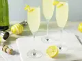 Trzy kieliszki musującego drinka French 75, jeden na ginie, drugi na koniaku, z cytrynową dekoracją.