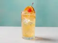 Orzeźwiający John Collins drink z lodem, plasterkiem pomarańczy i wisienką na tle turkusowej ściany.