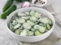 Mizeria ze śmietaną lub jogurtem naturalnym, z dodatkiem koperku i czerwonej cebuli, podana w białej misce.