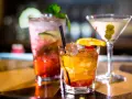 Kolorowe drinki z wódką smakową: czerwony z ogórkiem i miętą, bursztynowy z pomarańczą i wiśnią, oraz martini z oliwkami.