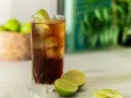 Orzeźwiający Cuba Libre, czyli rum z colą i limonką, z kostkami lodu i świeżymi limonkami w tle. Idealny na upalne dni.