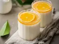 Panna Cotta przepis: dwa kremowe desery w szklankach, ozdobione plasterkiem pomarańczy i galaretką. Idealne na letnie popołudnie.