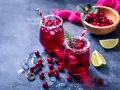 Dwa orzeźwiające drinki z grenadiną, ozdobione żurawiną i rozmarynem, z limonką w tle.
