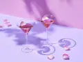 Elegancki Martini przepis: dwa kieliszki z różowym drinkiem, ozdobione płatkami róż, na fioletowym tle.