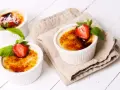Trzy kremowe desery, Crème brûlée czy crema catalana, ozdobione truskawkami i miętą, kuszą skarmelizowanym cukrem.