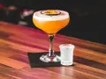 Orzeźwiający drink z marakują, ozdobiony plasterkiem owocu, stoi obok kieliszka z wodą gazowaną na drewnianym blacie.