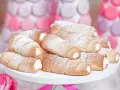 Domowe rurki z kremem, posypane cukrem pudrem, wyglądają apetycznie obok pastelowych dekoracji.