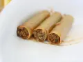 Trzy cannoloni z farszem mięsnym, wyglądające jak naleśniki z mięsem, leżą na białym talerzu.