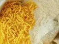 Ryż vs makaron: obok siebie leżą dwa rodzaje produktów. Z worka wysypano biały ryż, a obok niego spiralne fusilli i długie spaghetti.