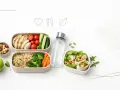 Zdrowe pudełka na lunch vs. tradycyjny obiad. Dwa pojemniki z kurczakiem, warzywami, kaszą, wrapami, butelką wody i jabłkiem.
