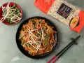 Gotowy **Chow Mein przepis** na talerzu: makaron z warzywami i kiełkami fasoli, obok paczka makaronu i miseczka kiełków.