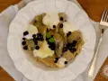 Knedle ze śliwkami czy pierogi z jagodami? Na talerzu pyszne pierogi z jagodami, polane śmietaną i posypane świeżymi owocami.