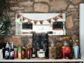 DIY drink bar z butelkami alkoholu, sokami i dzbankami z napojami. Tabliczka "ZRÓB TO SAM" zachęca do tworzenia własnych drinków.