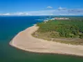 Widok z lotu ptaka na piaszczystą plażę, las i miasteczko nad morzem.
