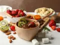 Jak zrobić fondue czekoladowe: zanurzaj truskawki i kiwi w gorącej czekoladzie. Na stole owoce, pianki i migdały.