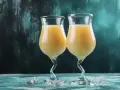 Dwa kieliszki z kremowym drinkiem z likieru bananowego, ozdobione kostkami lodu na turkusowym blacie.