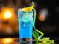 Niebieski koktajl z granatem, lodem, plasterkiem limonki i ozdobną skórką cytrynową.