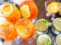 Orzeźwiający drink z prosecco, udekorowany plasterkiem pomarańczy, czeka na gości. Obok inne napoje z miętą i cytryną.