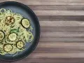 Penne z cukinią na ciemnym talerzu, ozdobione grillowanymi plasterkami cukinii. Danie wygląda apetycznie i lekko.