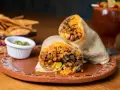 Pyszny burrito przepis: soczyste mięso, ryż, fasola i awokado zawinięte w tortillę. Obok chipsy i sos.