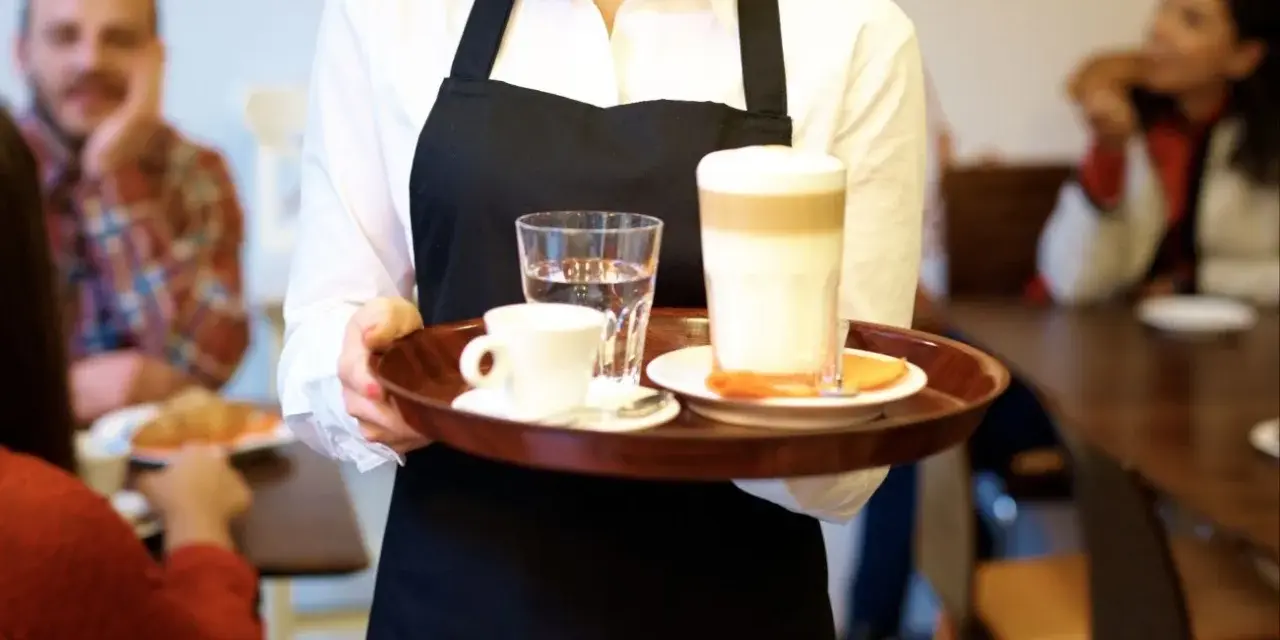 Kelnerka niesie tacę z kawą i wodą. Zastanawiasz się, ile zarabia barman w Sopocie?