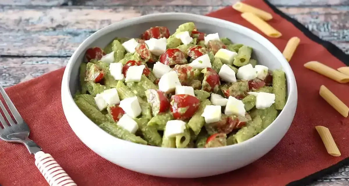 Makaron z pesto ze słoika przepis: penne z zielonym pesto, pomidorkami koktajlowymi i kostkami mozzarelli w białej misce.