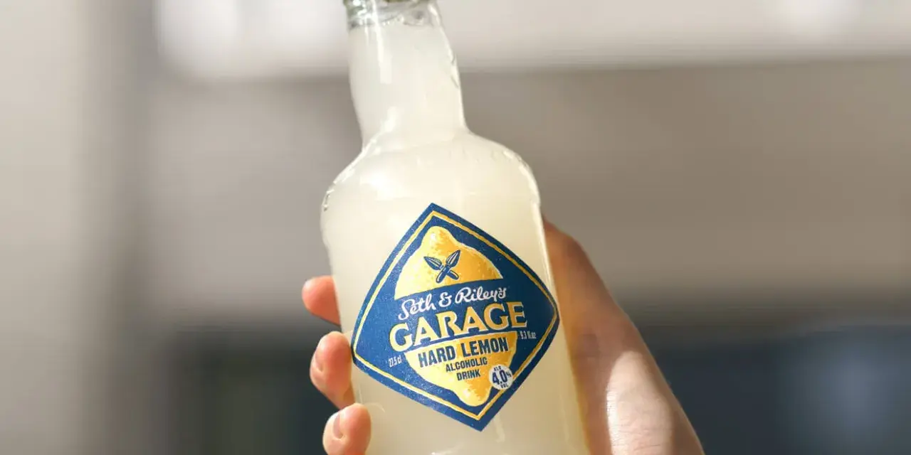 Ręka trzyma butelkę Seth & Riley's GARAGE Hard Lemon, orzeźwiający drink z piwem.